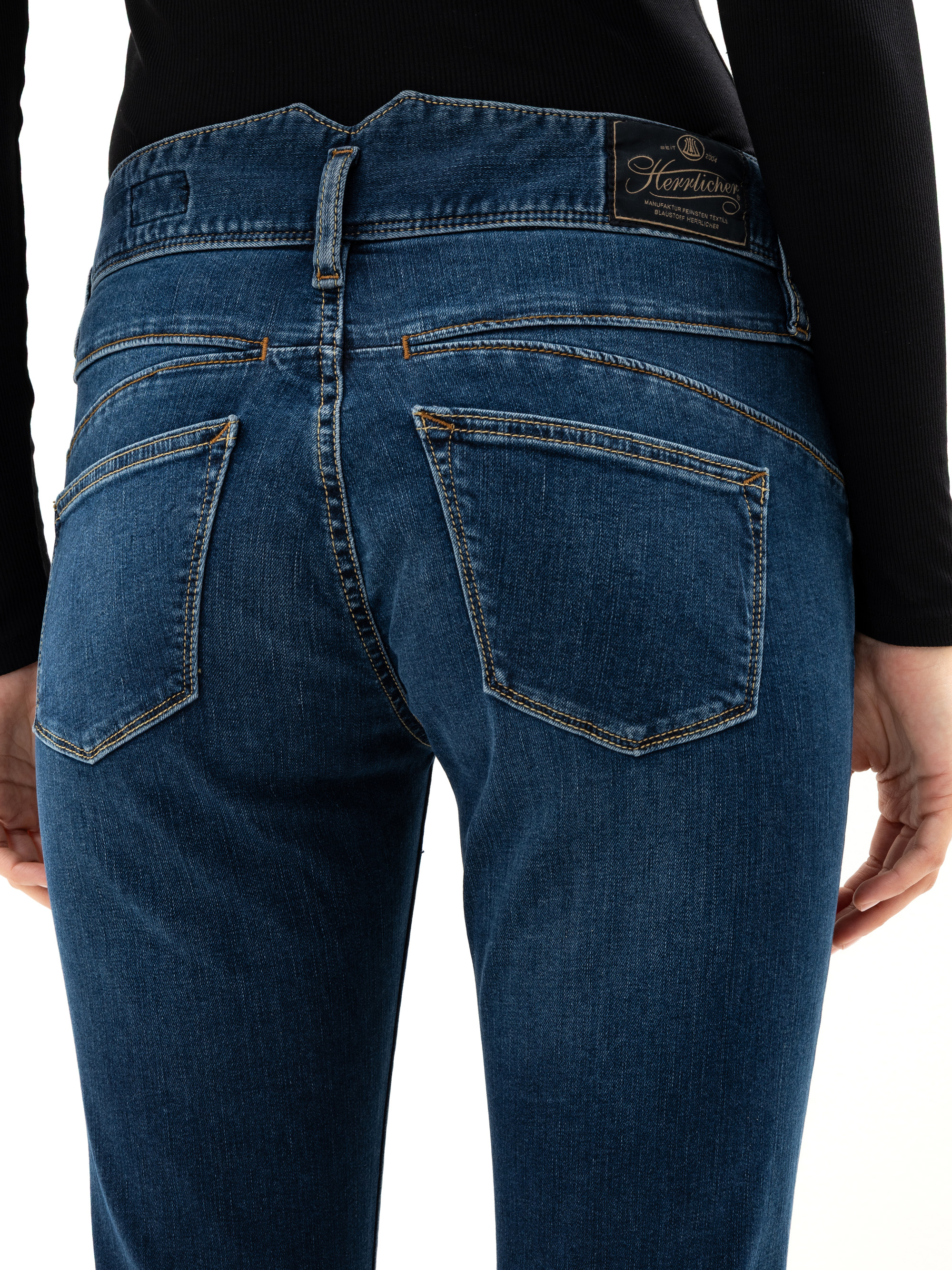 Nahaufnahme einer Person, die eine blaue Jeans und ein schwarzes langärmeliges Oberteil trägt, von hinten gesehen. Die Jeans hat zwei Gesäßtaschen und ein schwarzes Etikett am Bund.