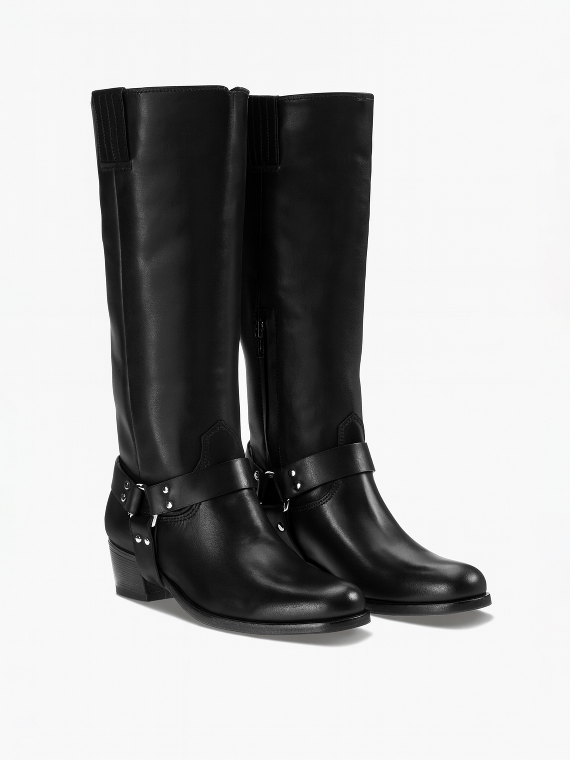 Ein Paar hohe, schwarze Lederstiefel mit niedrigem Absatz und dekorativen Riemen mit silbernen Nieten, fotografiert auf weißem Hintergrund.