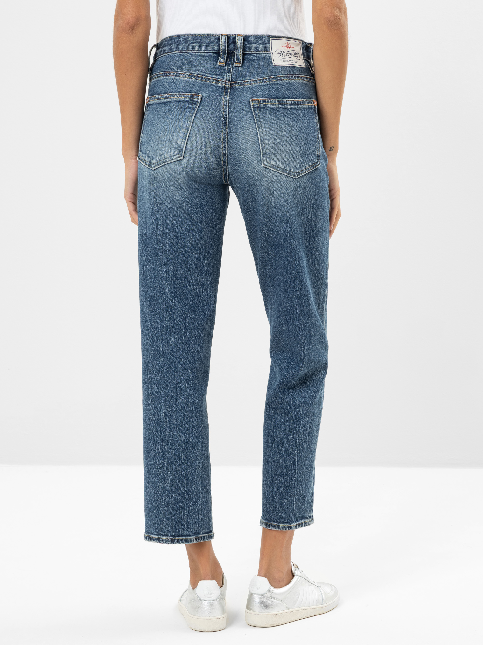 Eine Person, die eine blaue Jeans mit geradem Bein und weiße Turnschuhe trägt, steht mit dem Rücken zur Kamera und zeigt die Gesäßtaschen und die verblassten Details der Jeans.