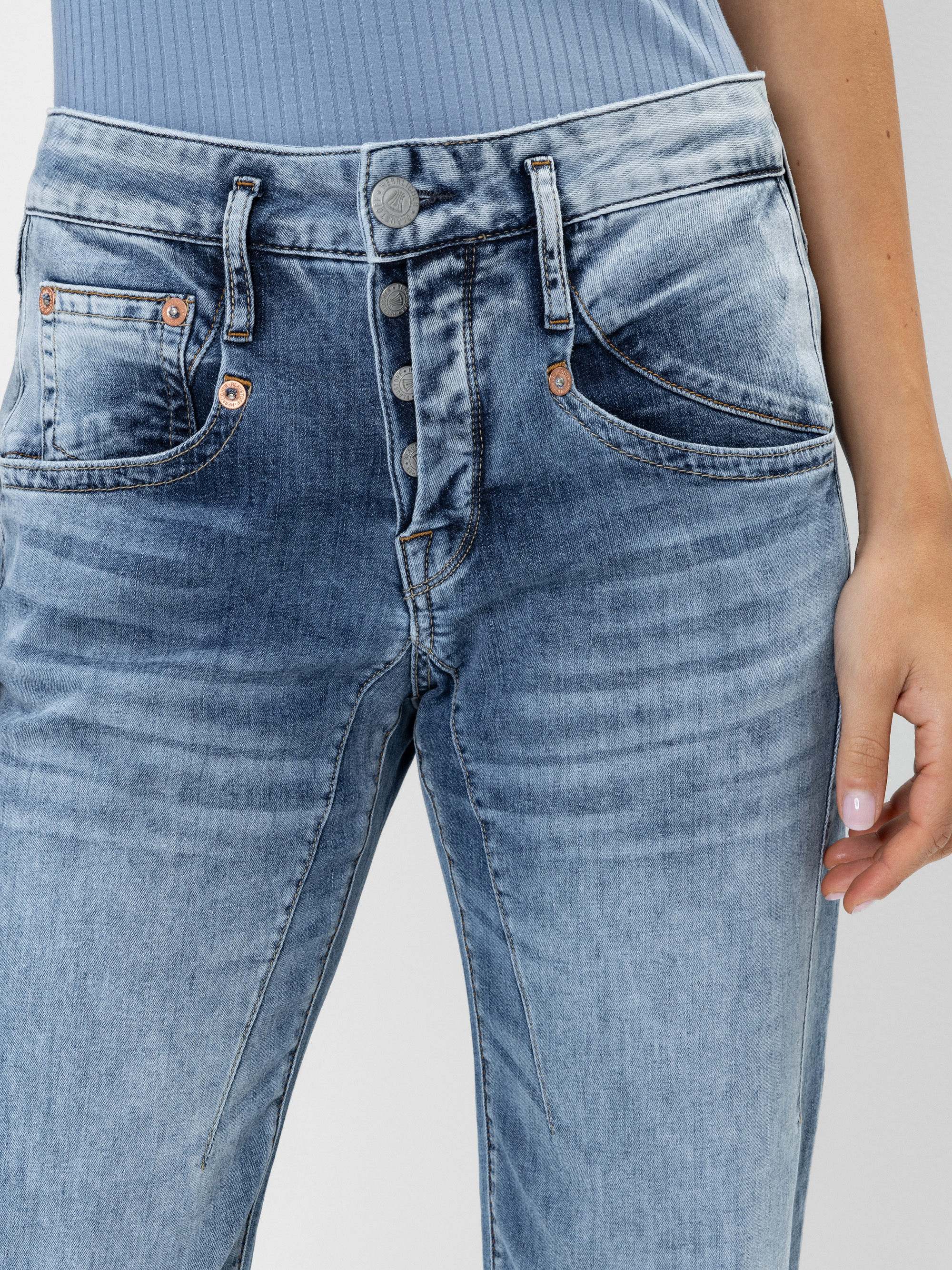 Eine Person trägt eine hellblaue, hochtaillierte Jeans mit Knopfleiste und ein hellblaues, geripptes Oberteil. Die rechte Hand der Person ruht an ihrer Seite. Die Jeans sieht verblasst und abgenutzt aus.