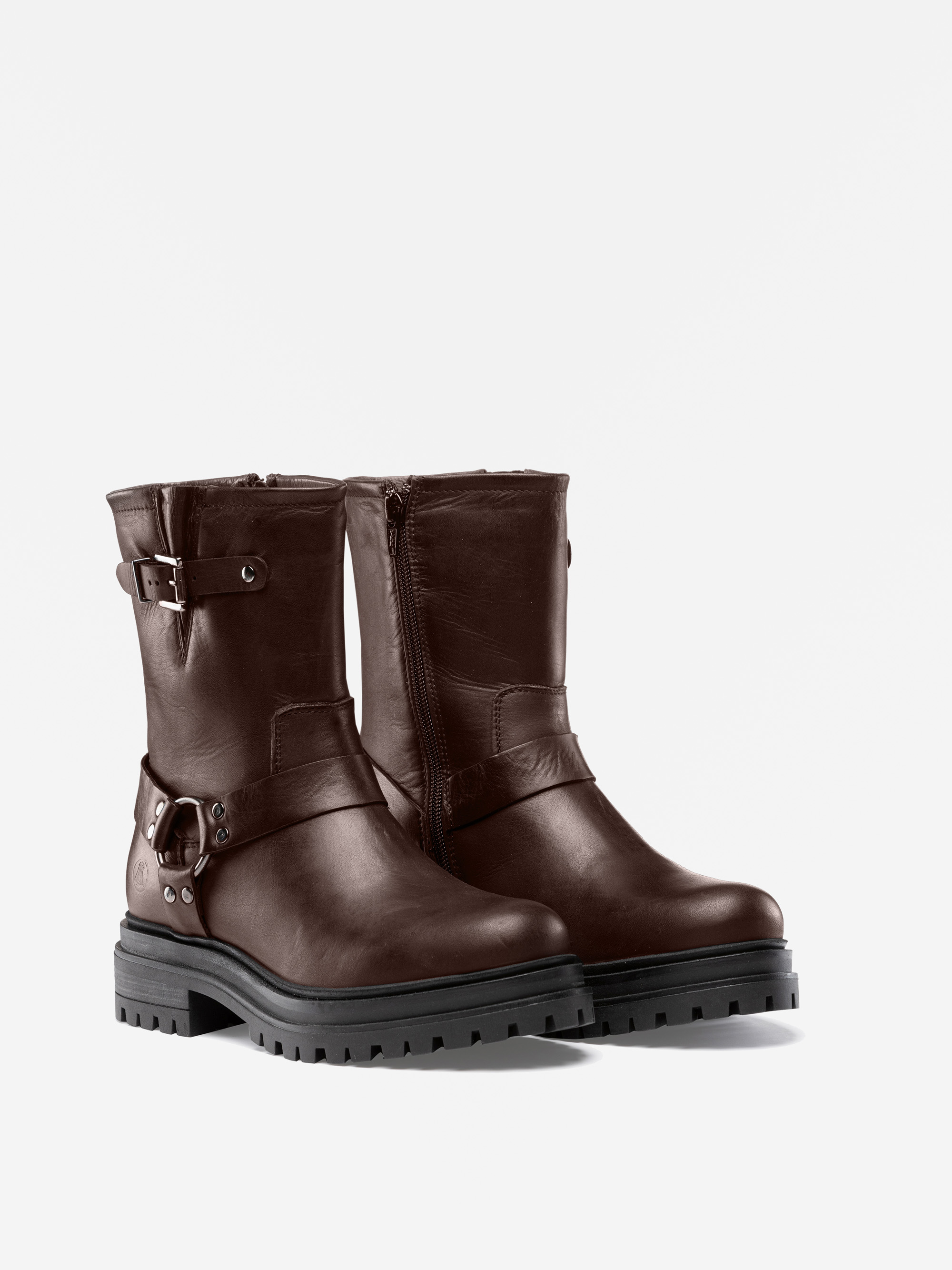 Ein Paar dunkelbraune Lederknöchelstiefel mit klobigen schwarzen Sohlen, seitlichen Reißverschlüssen, dekorativen Schnallen und Trageriemen, die vor einem schlichten weißen Hintergrund präsentiert werden.