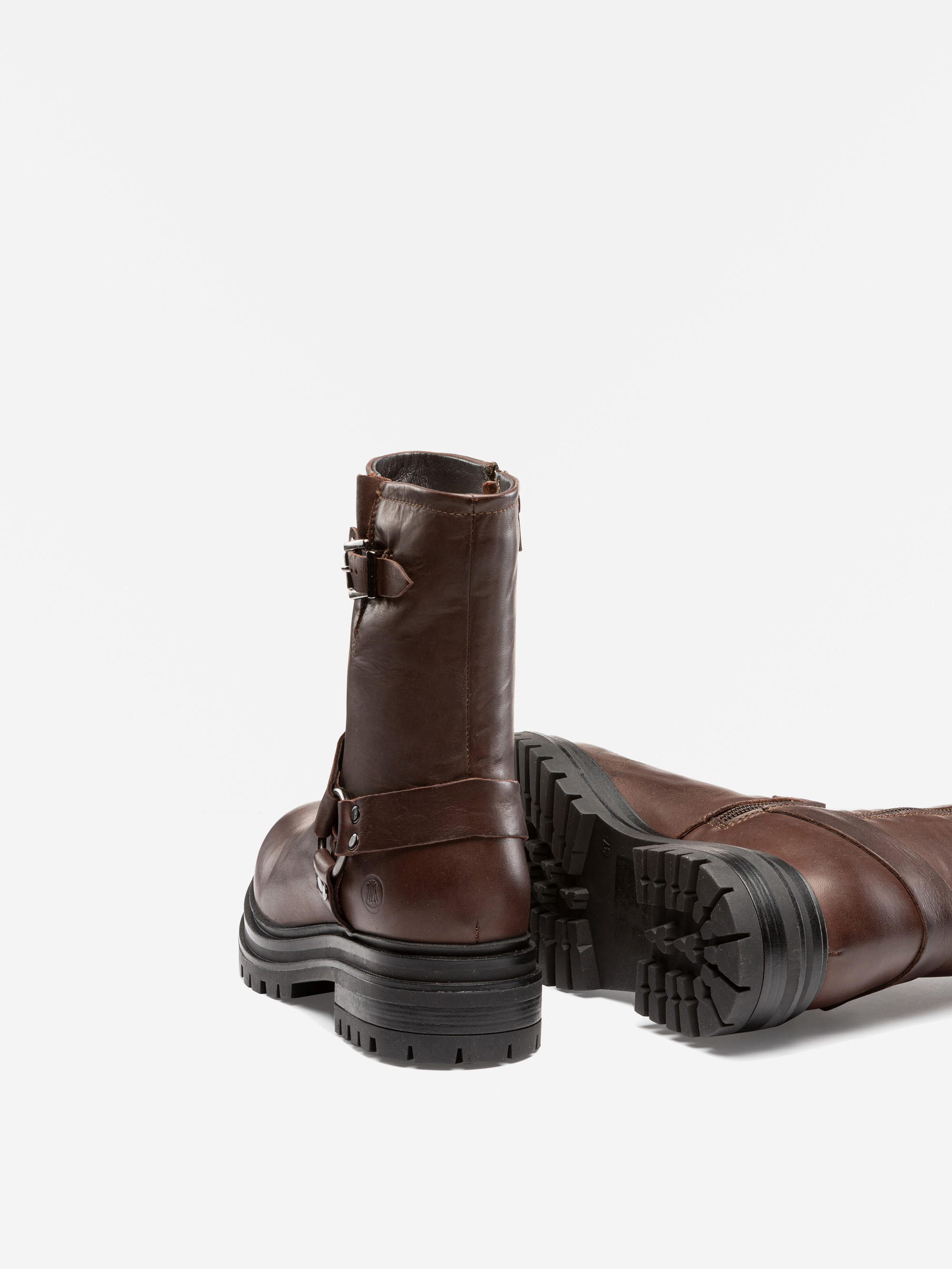 Ein Paar braune, halbhohe Lederstiefel mit klobigen schwarzen Gummisohlen. Ein Stiefel steht aufrecht und zeigt den Rücken und die seitlichen Schnallen, während der andere auf der Seite liegt und das Profil zeigt.