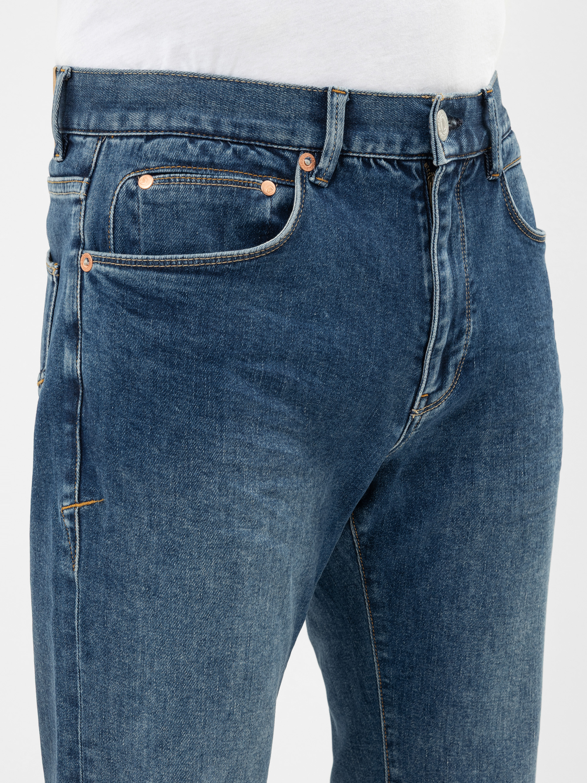 Nahaufnahme einer Person, die eine blaue Jeans und ein weißes Hemd trägt, wobei der Schwerpunkt auf der Taille und dem Oberschenkelbereich liegt, mit sichtbaren Nähten und Metallnieten an den Taschen der Jeans.
