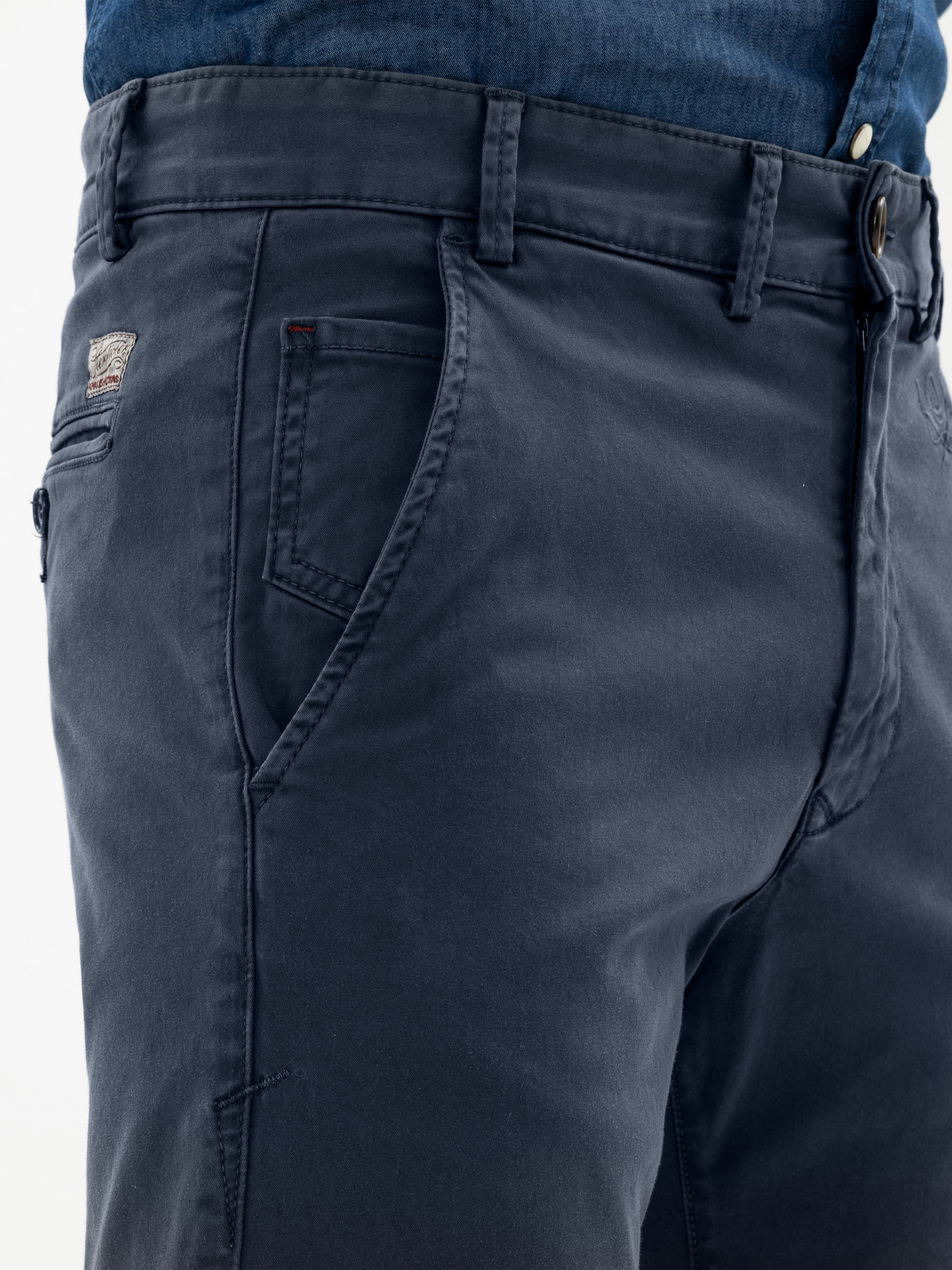Nahaufnahme einer Person, die eine dunkelblaue Hose und ein dazu passendes blaues Hemd trägt, wobei die Vordertasche, die Gürtelschlaufen und die Details am Bund zu sehen sind.