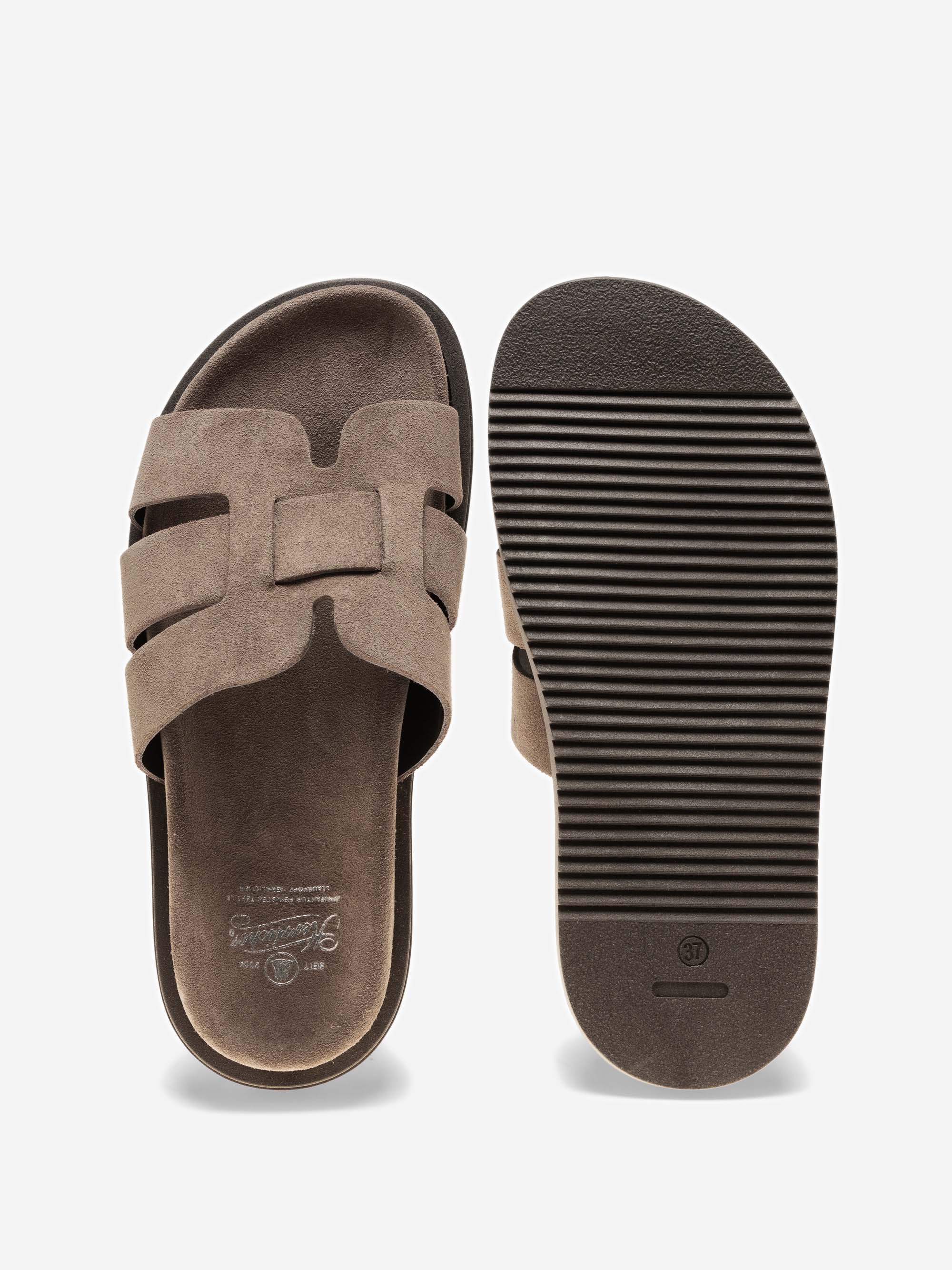 Ein Paar taupefarbene Gleitsandalen aus Wildleder; eine Sandale zeigt das Oberteil mit breiten Riemen und einem zentralen Ausschnitt, während die andere die geriffelte, strukturierte Sohle zeigt.