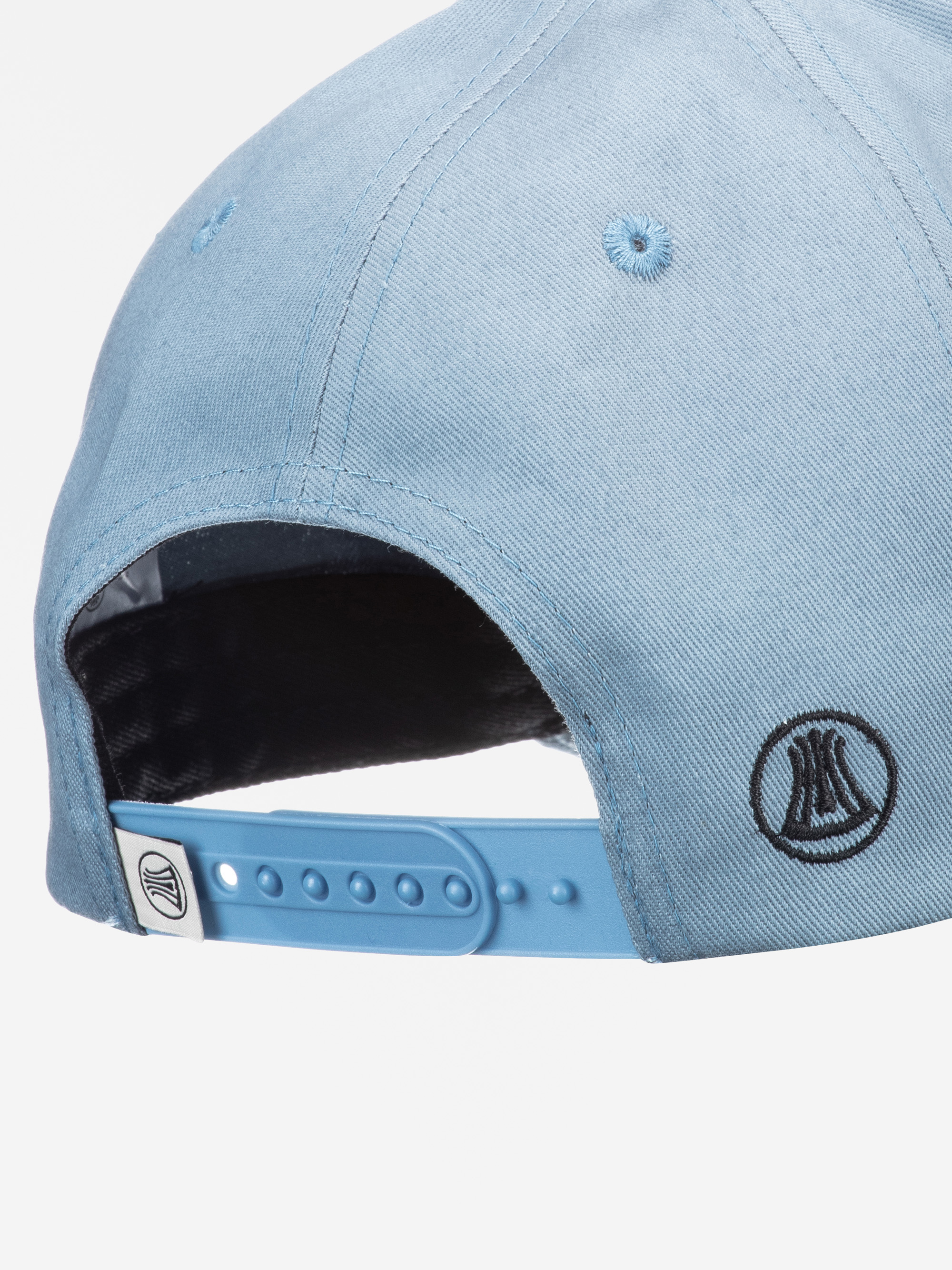 Nahaufnahme der Rückseite einer hellblauen Baseballmütze mit einem verstellbaren Snapback-Riemen und zwei schwarzen, kreisförmigen Logoaufnähern, einer über dem Riemen und einer auf dem Riemen selbst.