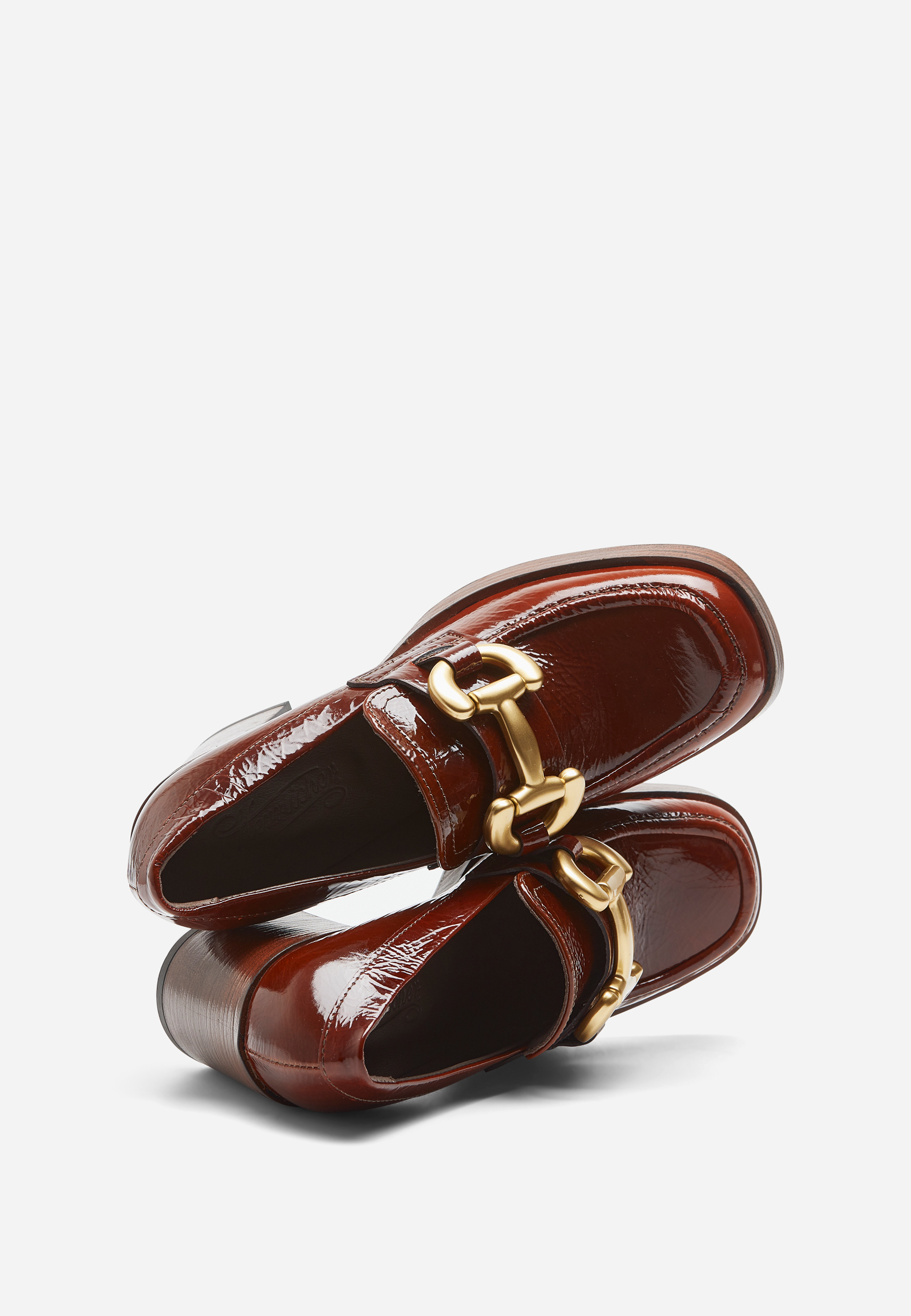 Ein Paar glänzender, dunkelbrauner Slipper mit klobigen goldenen Kettenakzenten auf der Vorderseite, die sich vor einem weißen Hintergrund präsentieren.