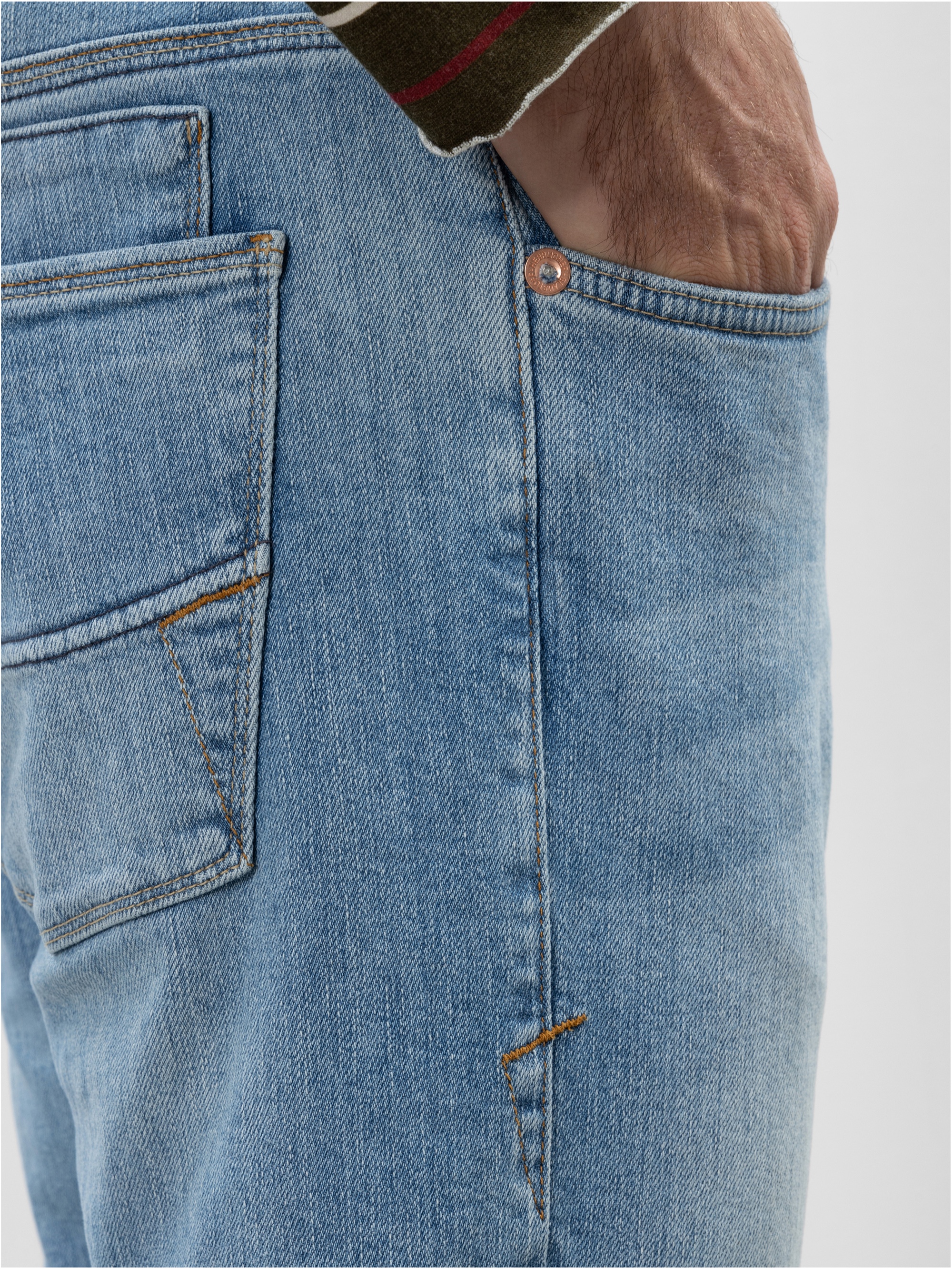 Nahaufnahme einer Person, die eine hellblaue Jeans trägt und ihre rechte Hand in die Vordertasche steckt. Die Nähte und die Textur des Jeansstoffs sind deutlich zu erkennen.