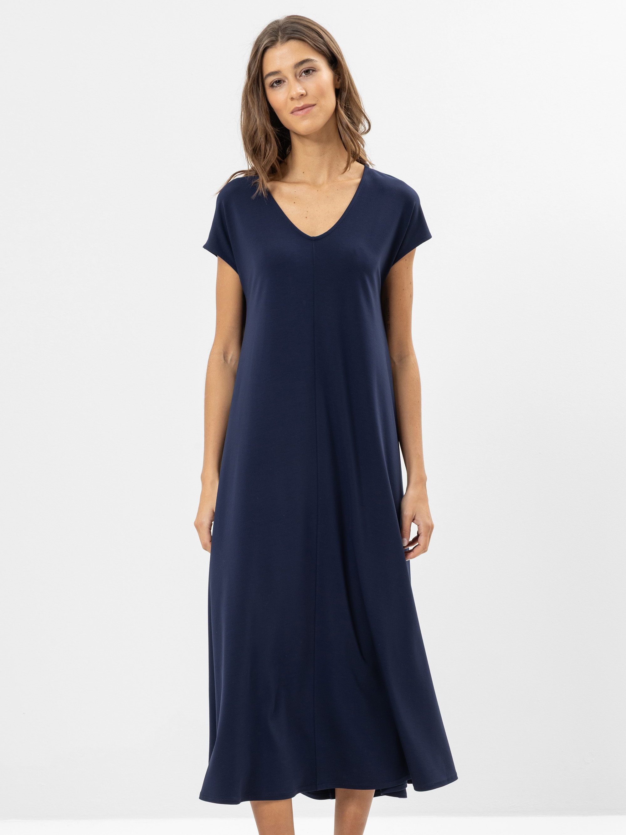 Eine Frau steht vor einem schlichten weißen Hintergrund und trägt ein locker sitzendes, kurzärmeliges, marineblaues Midikleid mit V-Ausschnitt. Sie hat schulterlanges braunes Haar und einen neutralen Gesichtsausdruck.